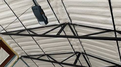 Closed cell spray foam insulation sprayed onto the underside of a corrugated metal roof between steel trusses